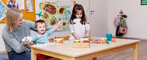 Mitarbeiterin betreut zwei Kinder beim Spielen am Basteltisch.