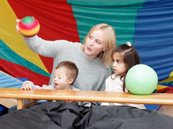 Mitarbeiterin spielt mit zwei Kindern in der Turnhalle mit Bällen.